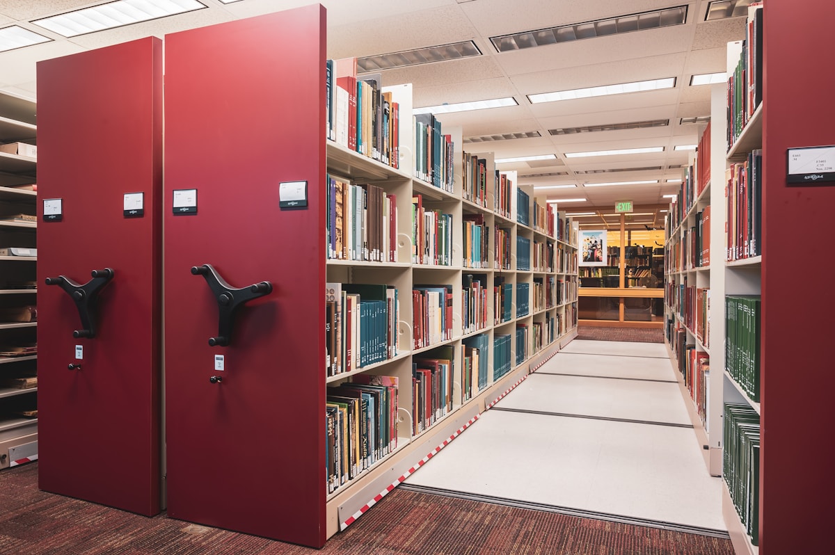 A long aisle of tall library shelves filled with books.
